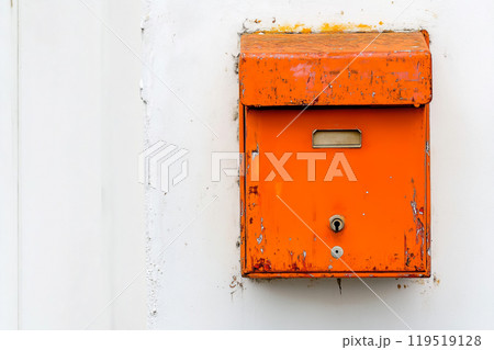An old, weathered orange mailbox mounted on a white wall, showcasing the effects of time and the 119519128