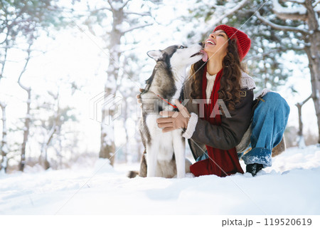 Young woman walking her dog in winter and both explore the snow together in playful mood. Friendship 119520619