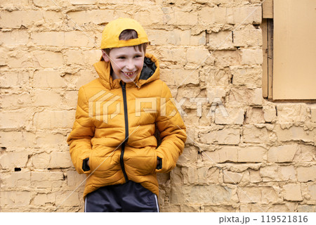 A child on the street. A happy boy is standing against a brick wall in yellow clothes and a baseball cap. 119521816