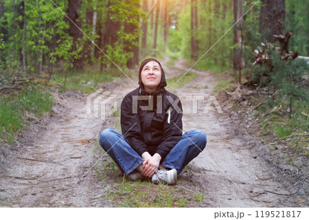 Man in the forest. A middle-aged woman sits on a forest road. 119521817