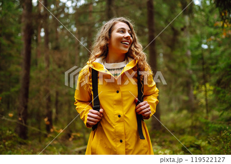 Traveler woman in yellow coat explores, walks through wild forest in nature. Vacation travel concept 119522127