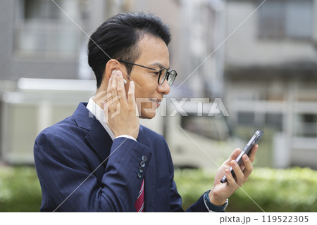 スマートフォンを見るイヤホンをつけた30代後半のビジネスマン　横顔 119522305