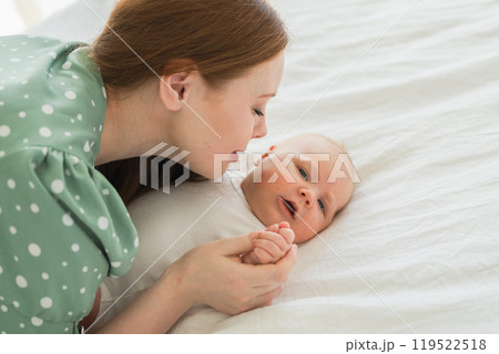 Happy family at home. Mother playing with little toddler child on bed. Mom baby relax playing having fun together. Mother looks at baby with love care. Mom of breast feeding baby rest in living room 119522518