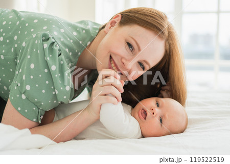 Happy family at home. Mother playing with little toddler child on bed. Mom baby relax playing having fun together. Mother looks at camera with love care. Mom of breast feeding baby rest in living room 119522519