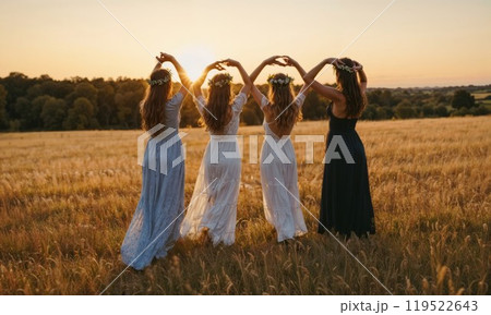 A group of women hold hands in a sunset field, embracing nature 119522643
