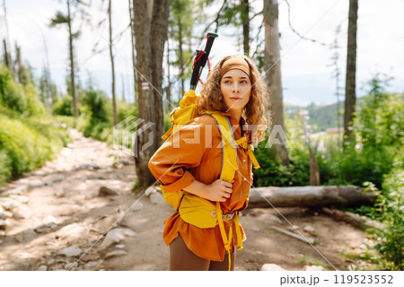 Woman traveler with yellow hiking backpack, hiking poles on trail among mountains. Adventure concept 119523552