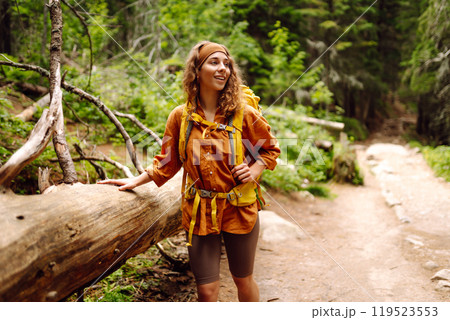 Traveler with yellow backpack walks along hiking path among mountains in the forest. Enjoys nature. 119523553