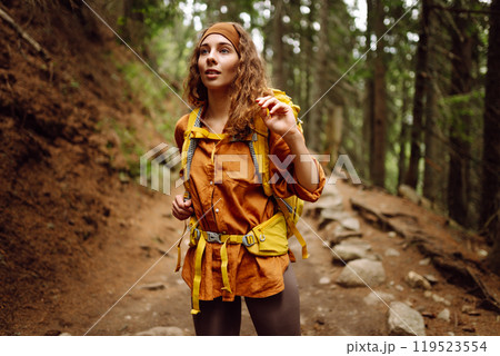 Traveler with yellow backpack walks along hiking path among mountains in the forest. Enjoys nature. 119523554