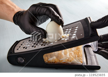 hands in black gloves grind a boiled egg on a metal grater 119523835