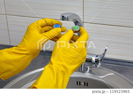 Plumber's hands in yellow rubber gloves change an old clogged kitchen sink faucet aerator to a new one Plumber's hands in yellow rubber gloves change an old clogged kitchen sink faucet aerator to a new one 119523965
