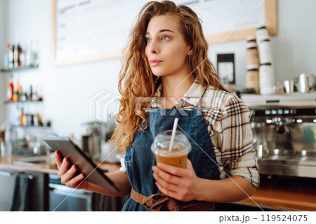 Portrait of a friendly female barista holding a tablet computer and smiling. Takeaway concept 119524075