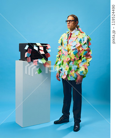 Office worker covered in sticky notes. Young man, employee in formal wear standing against blue background 119524490