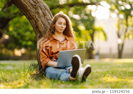 Young curly woman in the park on a green lawn with a laptop in her hands. Online education. 119524550