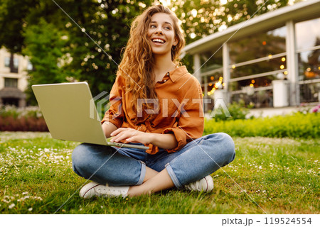 Young curly woman in the park on a green lawn with a laptop in her hands. Online education. Young curly woman in the park on a green lawn with a laptop in her hands. Online education. 119524554