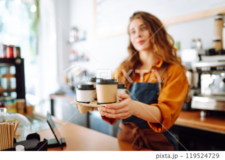 Young female barista holding disposable glasses with hot drink to go. Takeaway delivery concept. Young female barista holding disposable glasses with hot drink to go. Takeaway delivery concept. 119524729