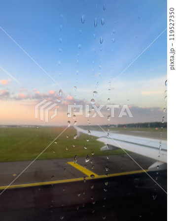 Rain Droplets on Airplane Window With View of Runway at Sunset During Departure From Airport 119527350