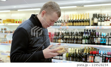 A man thoughtfully chooses products in a supermarket. Shopper carefully examines the label on a box of cookies in a supermarket aisle, contemplating their purchase 119528234