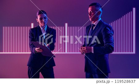 Two speaker, man and woman dressed formalwear, captivates audience with glowing data graphs during corporate seminar. Neon light. Two speaker, man and woman dressed formalwear, captivates audience with glowing data graphs during corporate seminar. Neon light. 119528637