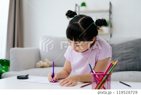 A young girl is sitting on a couch and drawing with color pencil. 119528729