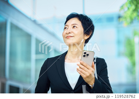 スマホを持って立つスーツ姿のミドルビジネスウーマン 119528762