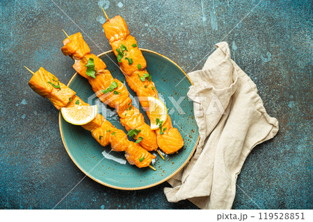 Grilled barbecue salmon skewers seasoned with green parsley and lemon on ceramic plate on dark blue concrete rustic table background top view, healthy eating Grilled barbecue salmon skewers seasoned with green parsley and lemon on ceramic plate on dark blue concrete rustic table background top view, healthy eating 119528851