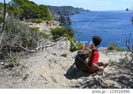 Young sporty man with backpack sitting on the top of rock and looking at the seashore and mountains 119528990