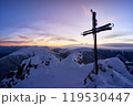 Majestic sunset over snowy mountain peak with cross silhouette, creating peaceful winter landscape 119530447