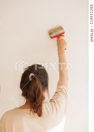 Woman holds brush with glue against light wall apply thick wallpaper glue. Ready to paste wallpaper Woman holds brush with glue against light wall apply thick wallpaper glue. Ready to paste wallpaper 119531288
