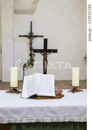 A church altar with a cross, candles, flowers, and an open bible 119532189
