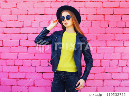 Fashion young woman wearing a black hat, jacket on colorful pink bricks background 119532733