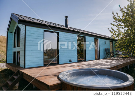 Modern wooden cabin with outdoor hot tub on a sunny deck, ideal for relaxing getaways 119533448