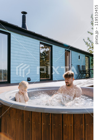 Father and son bonding in backyard hot tub, splashing water, enjoying outdoor family time under sun 119533455