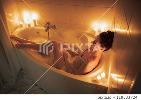 A woman is sitting in a bathtub with candles lit around her. Scene is relaxing and calming. A woman is sitting in a bathtub with candles lit around her. Scene is relaxing and calming. 119533724