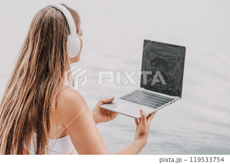 A woman is sitting by the water with a laptop in her lap 119533754