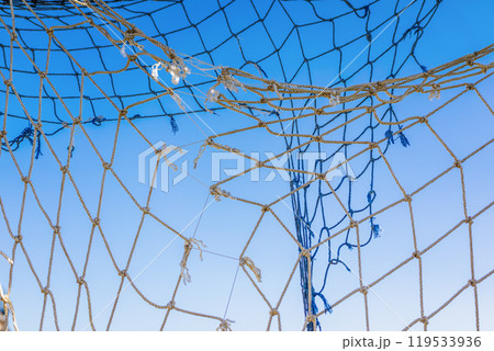 Close up of old fishing net against a clear blue sky Close up of old fishing net against a clear blue sky 119533936