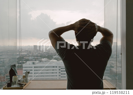 Lonely single man looking out to through the windows of apartment. 119538211