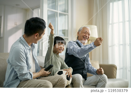 asian son father grandfather watching soccer game on TV together at home 119538379