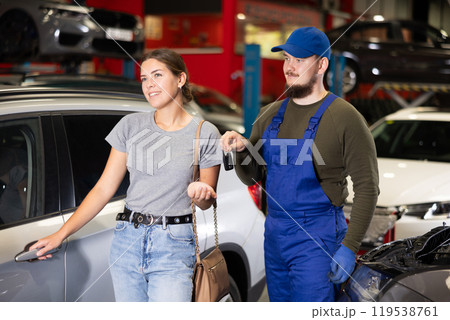 Young male mechanic giving car keys to woman client Young male mechanic giving car keys to woman client 119538761