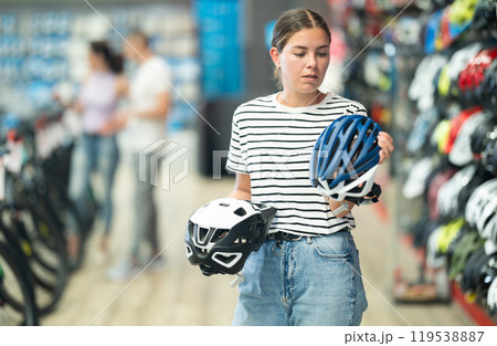 Young girl comparing two bicycle helmets in specialized shop 119538887