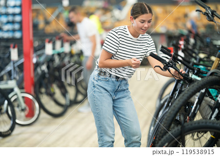 Smiling female shopper inspecting mountain bicycle handlebars in store 119538915
