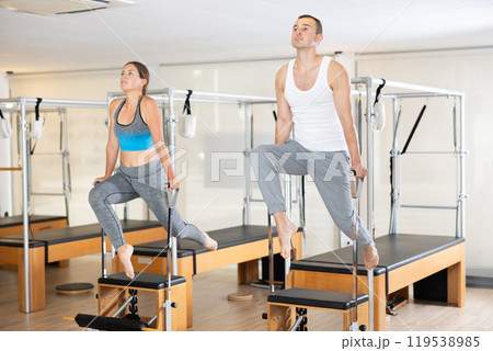Young man and woman performing Pilates exercises on Wunda chairs 119538985