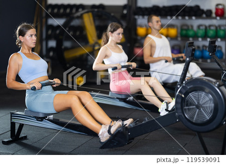 Athletic woman in sportswear training on rowing machine in sport gym 119539091