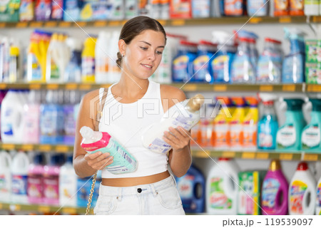 Woman carefully selects cleaning product in industrial section of supermarket 119539097