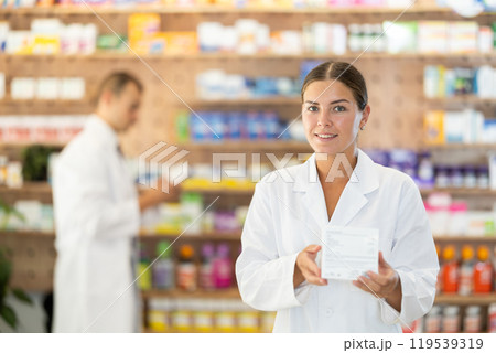 Female consultant pharmacist holds box in hands and offers to purchase remedy to alleviate condition Female consultant pharmacist holds box in hands and offers to purchase remedy to alleviate condition 119539319