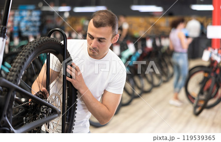 Experienced cyclist examining wheel while choosing bicycle in shop Experienced cyclist examining wheel while choosing bicycle in shop 119539365
