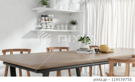 A close-up of a wooden dining table with home decor in a minimalist white dining room. A close-up of a wooden dining table with home decor in a minimalist white dining room. 119539758
