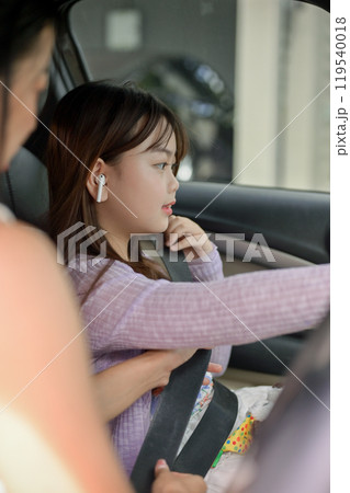 A caring Asian mom is fastening the seatbelt for her daughter before starting their family trip. 119540018