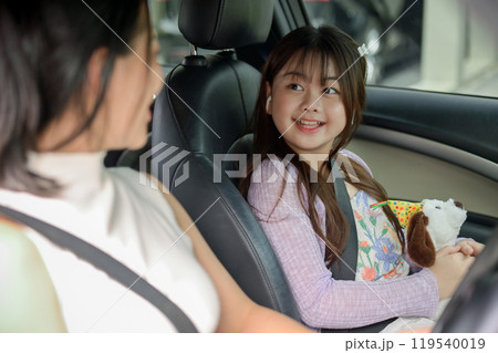 An adorable Asian girl happily chats with her mom during their family trip or on the way to school. 119540019