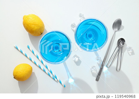 Blue cocktail in glass, whole lemons, straws and spoons on white background, top view Blue cocktail in glass, whole lemons, straws and spoons on white background, top view 119540968