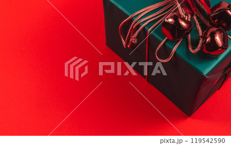 Green gift box with bells and bow on red background close up 119542590